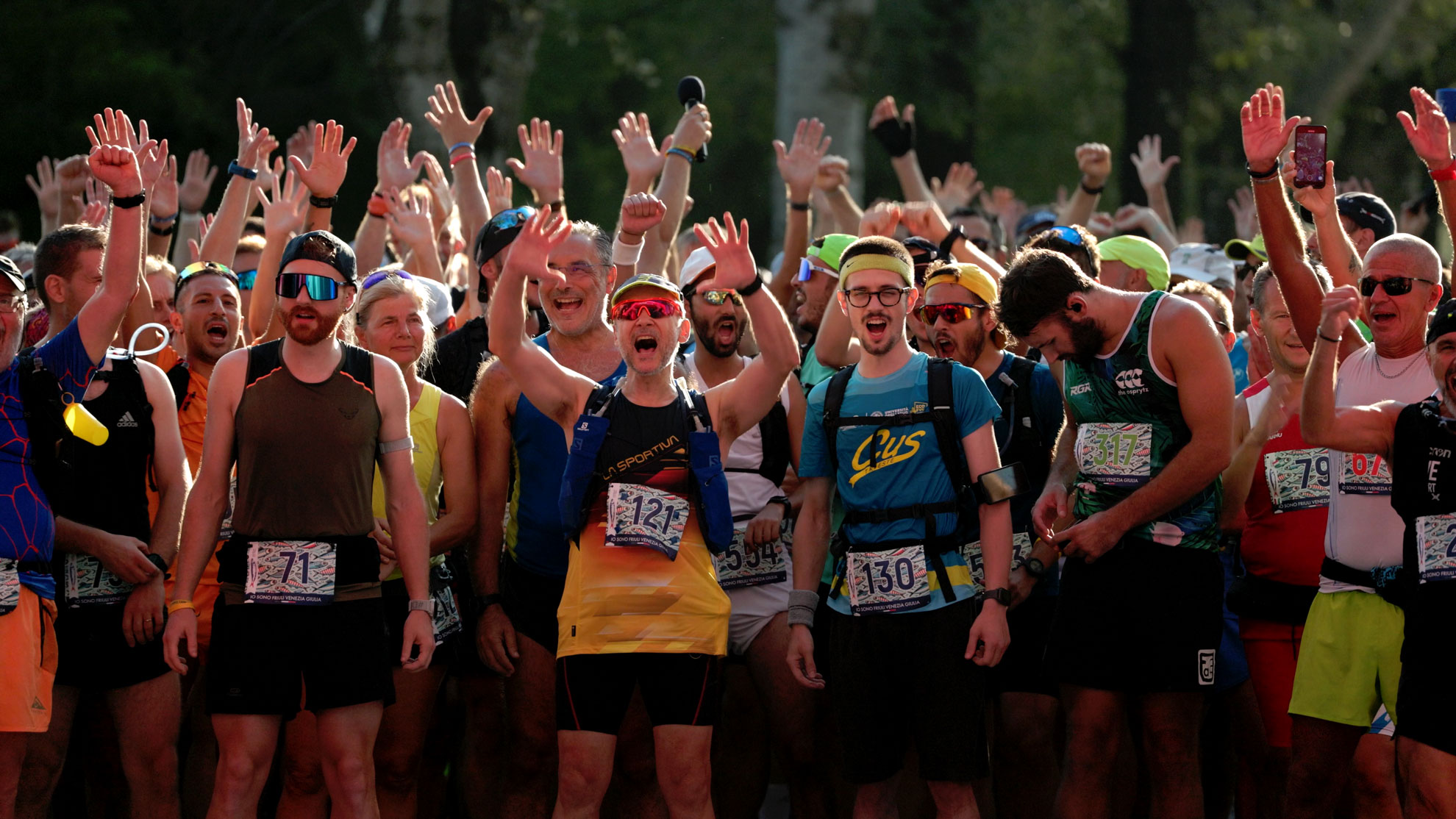 Runner al via della Sardon Run con le mani alzate al tramonto tra gli alberi