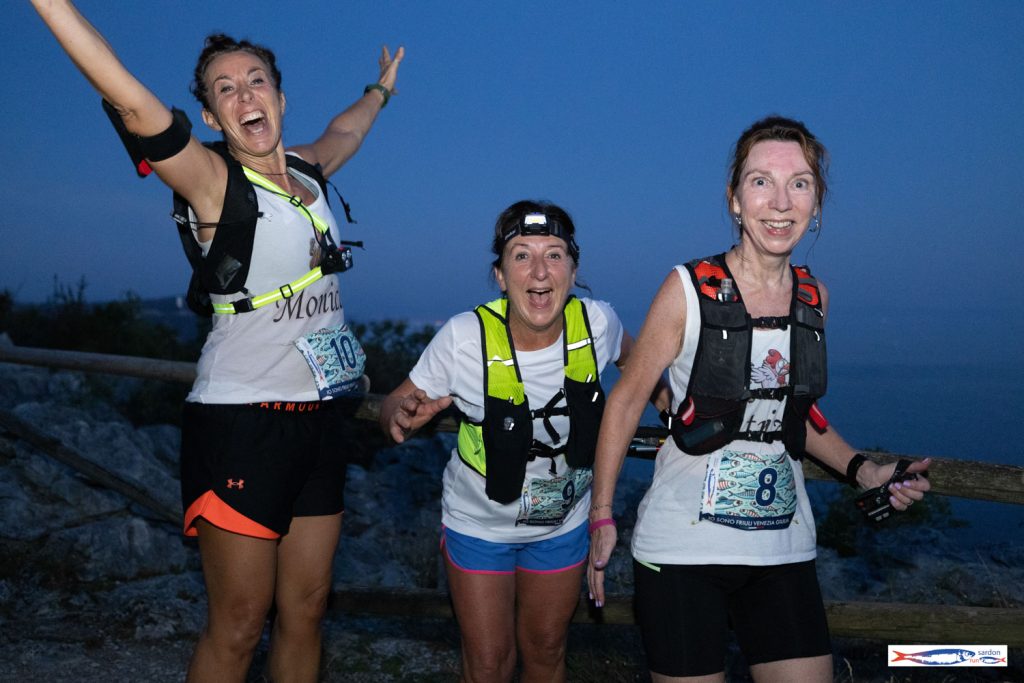 Tre trail runner con lampade frontali festeggiano all'ora blu sopra il Golfo di Trieste — Sardon Run