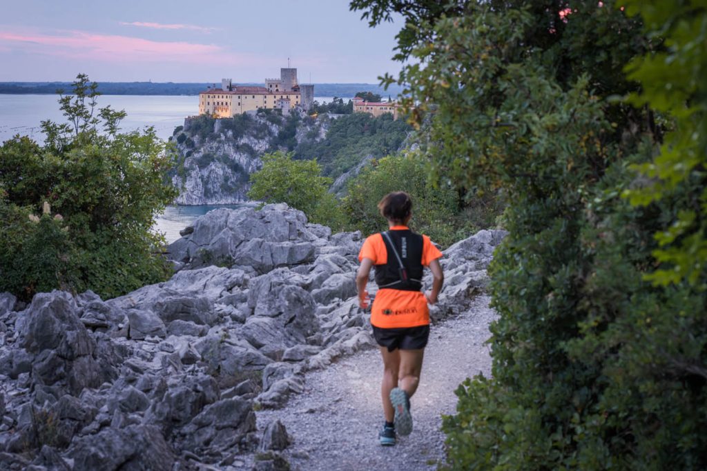 Trail runner sulla pietraia carsica con il Castello di Duino sullo sfondo al crepuscolo — Sardon Run