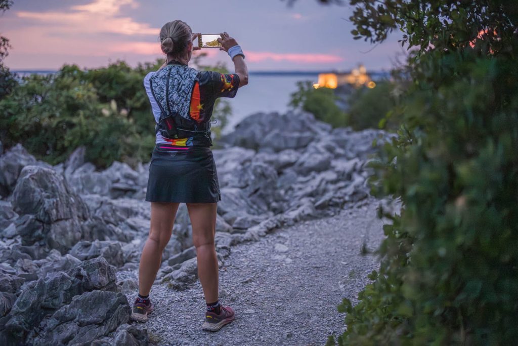 Una partecipante fotografa il tramonto sul mare dal sentiero carsico durante la Sardon Run