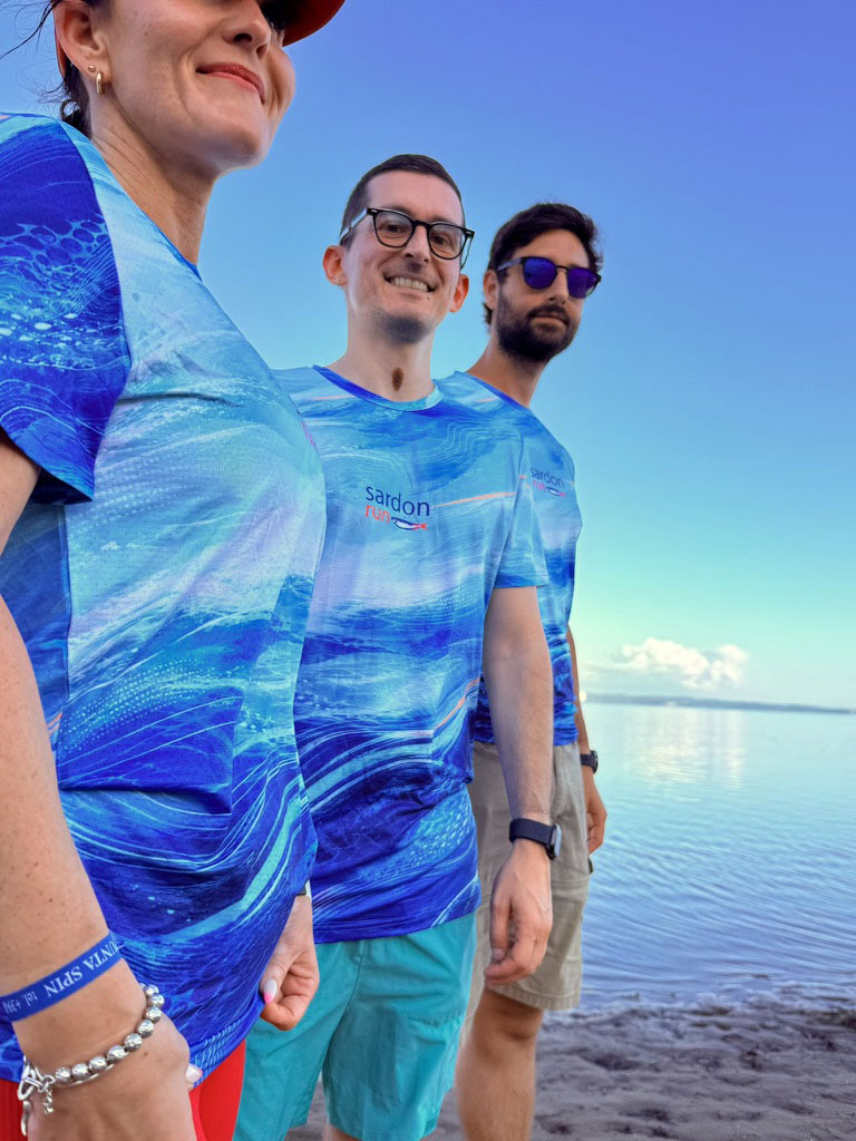 Maglietta tecnica Sardon Run 2026 — tre atleti in corsa sulla spiaggia