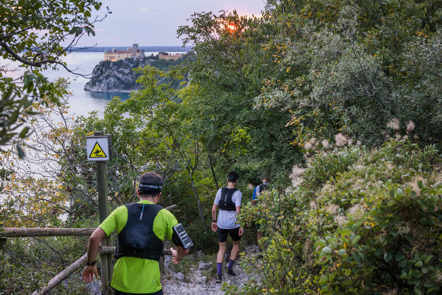 Runner in discesa sul Sentiero Rilke al crepuscolo, con il castello di Duino a picco sul mare